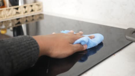 a woman cleans a black stove top with a blue cleaning cloth