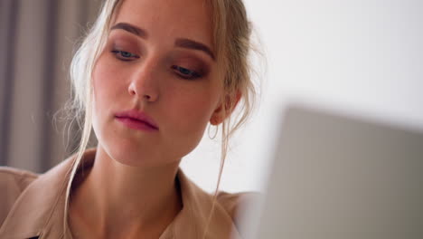 focused blonde woman looks at screen of modern laptop