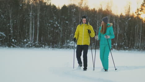 in the winter forest at sunset loving couple skiing and look around at the beauty of nature and attractions in slow motion.