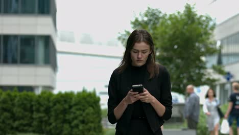 a young woman with brown hair walks towards the camera, looking intensely at her mobile phone