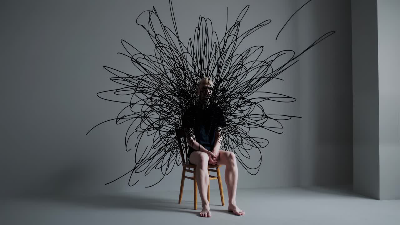 Psychological distress visualization showing seated male experiencing mental chaos, dark scribbles obscuring upper body and representing inner emotional turmoil against minimalist gray background
