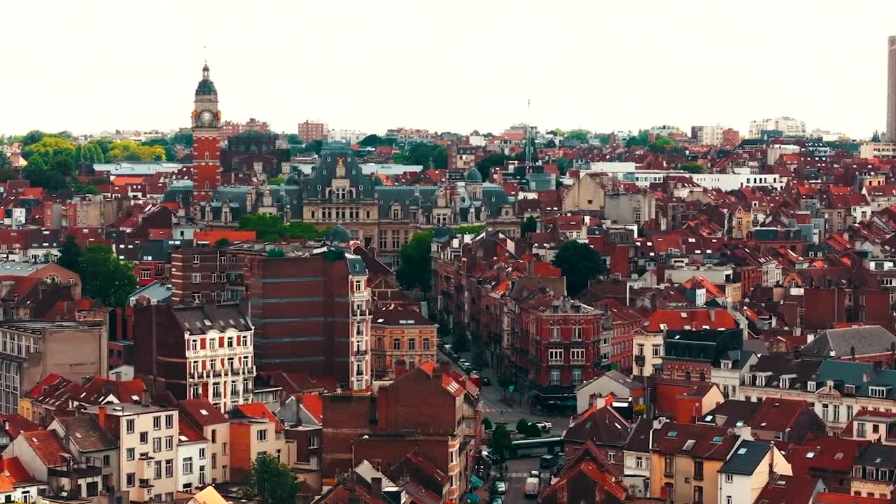 Gorgeous aerial drone footage flying over central city of Brussels or Bruxelles during a sunny day while a large church tower is visible in between red rooftops and historic apartment building houses.