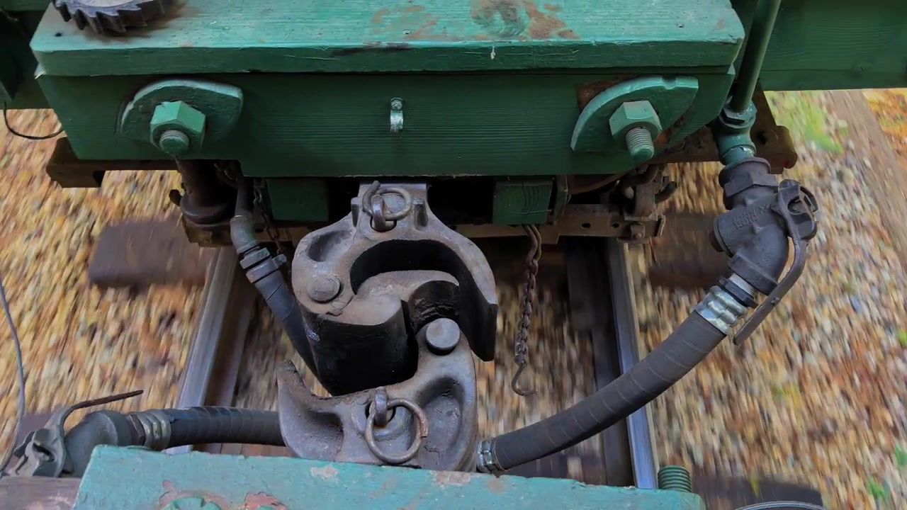 Close-up view of a train coupler and mechanical connections working between passenger cars as the railway carriage moves along the tracks, showing the coupling system in operation.