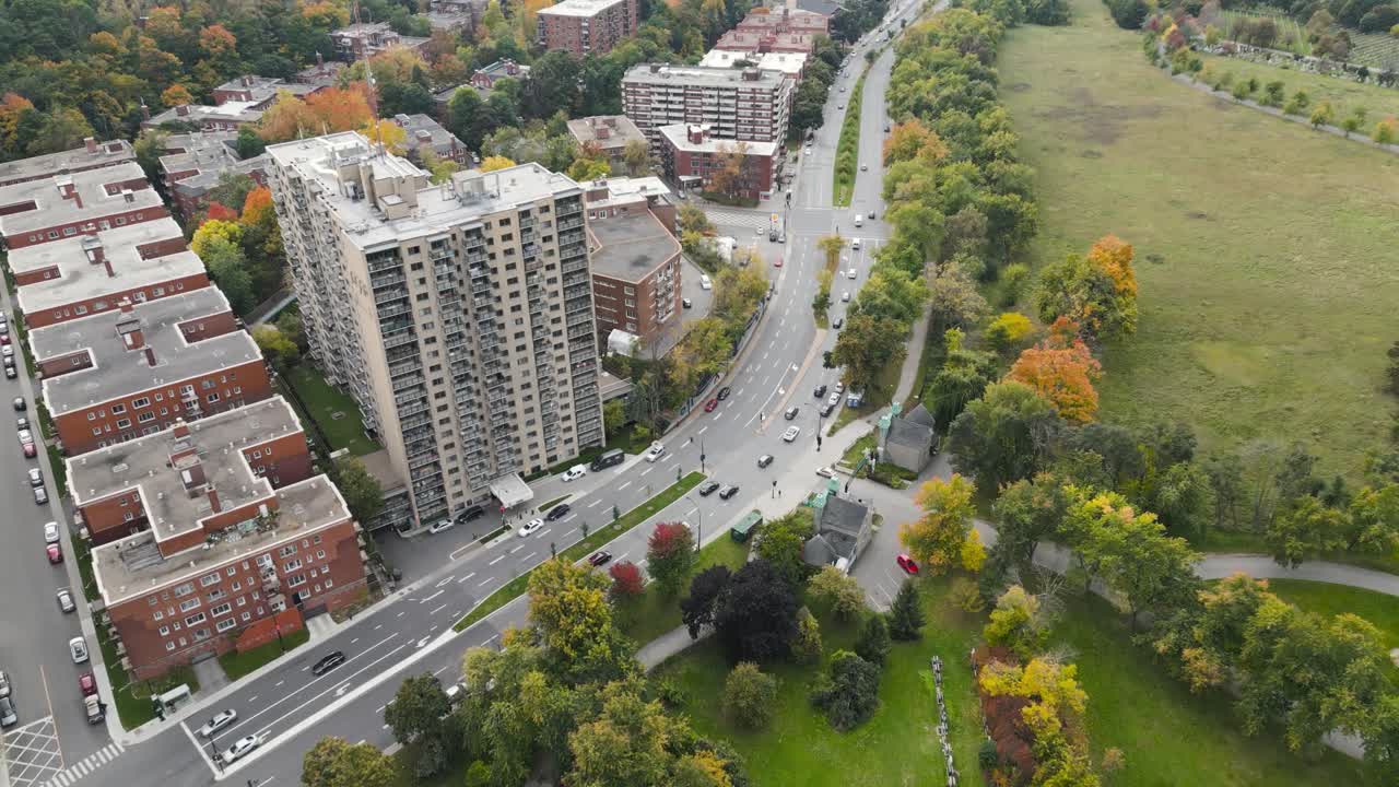 Autumn residential blocks line curving arterial road near Parc La Fontaine in Plateau Mont Royal district as trees show bright seasonal colors captured from clear aerial drone perspective