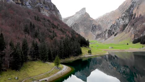 Aerial-flyover-from-the-shore-of-Seealpsee-in-Appenzell,-Switzerland-up-above-the-lake-revealing-reflection-of-the-Alpstein-peaks