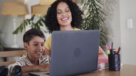 Biracial-boy-with-mother-learning-online-using-laptop-at-table,-slow-motion