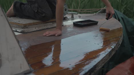 joven sellando la proa de la cubierta de barco de madera rodando sobre el barniz