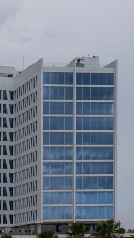 clouds passing in reflection of glass windows of skyscraper building in vertical