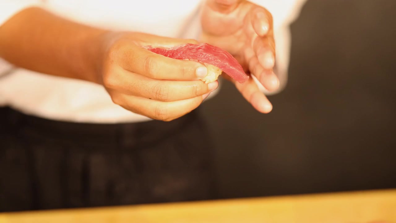 Close-up of a chef's hands skillfully shaping raw tuna over rice in Bangkok, Thailand.