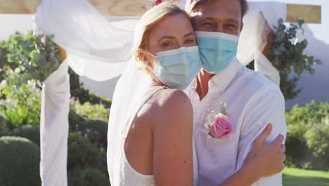 Portrait-of-happy-caucasian-newly-wed-couple-touching-heads-at-altar,-wearing-face-masks