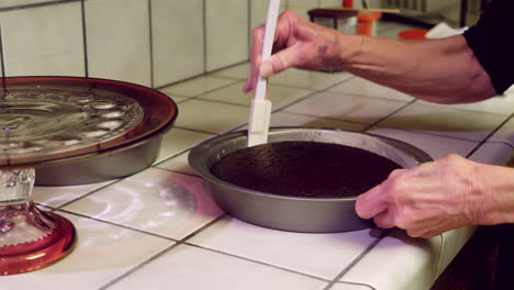 an elderly woman takes a chocolate cake out of a round baking pan after baking with a rubber spatula in the kitchen