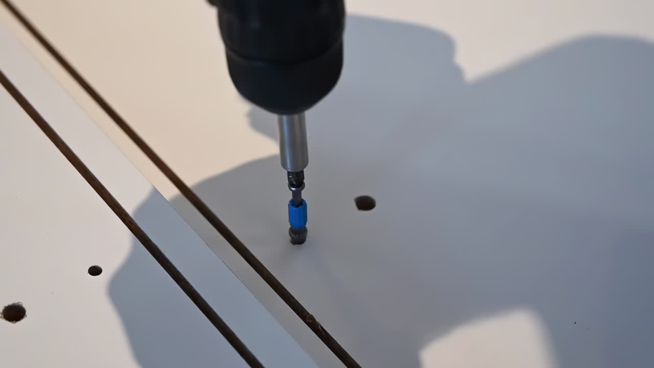 Close up of a man installing a a screw into a wooden table with a drill