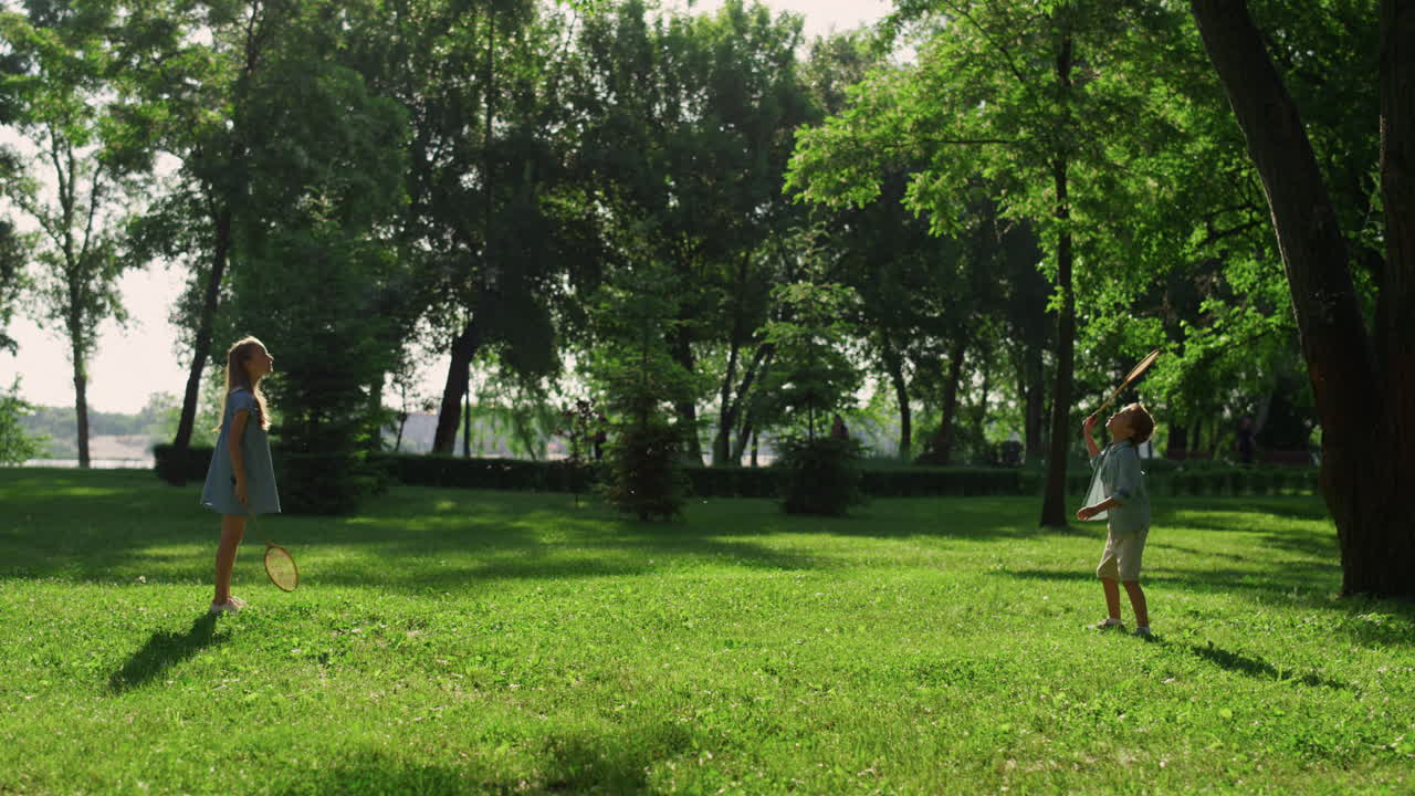la hermana mayor golpeando la lanzadera con la raqueta. el hermano pequeño no regresa