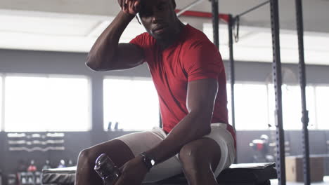 resting on gym bench, man in red shirt holding water bottle after workout