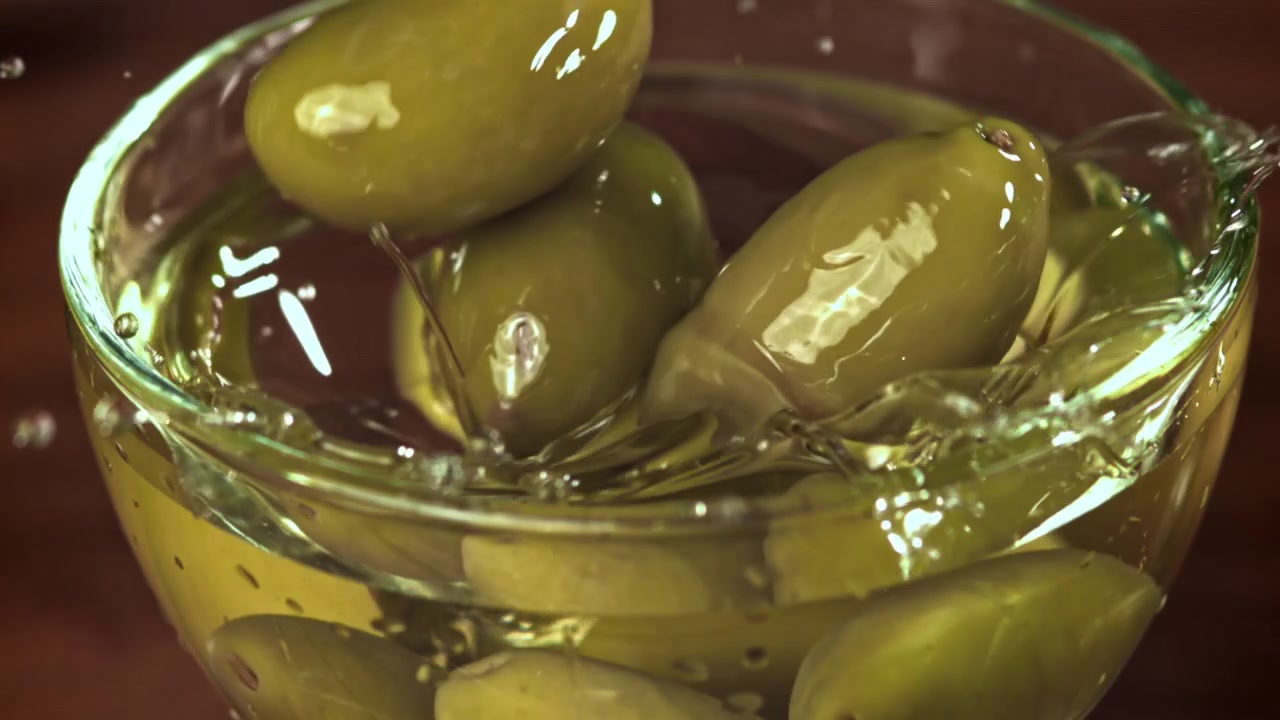 Olive verdi che cadono al rallentatore in una ciotola di vetro