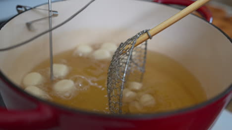 dejando caer bolas de masa de agujeros de donut en aceite de freír profundo con colador, cierre de cámara lenta