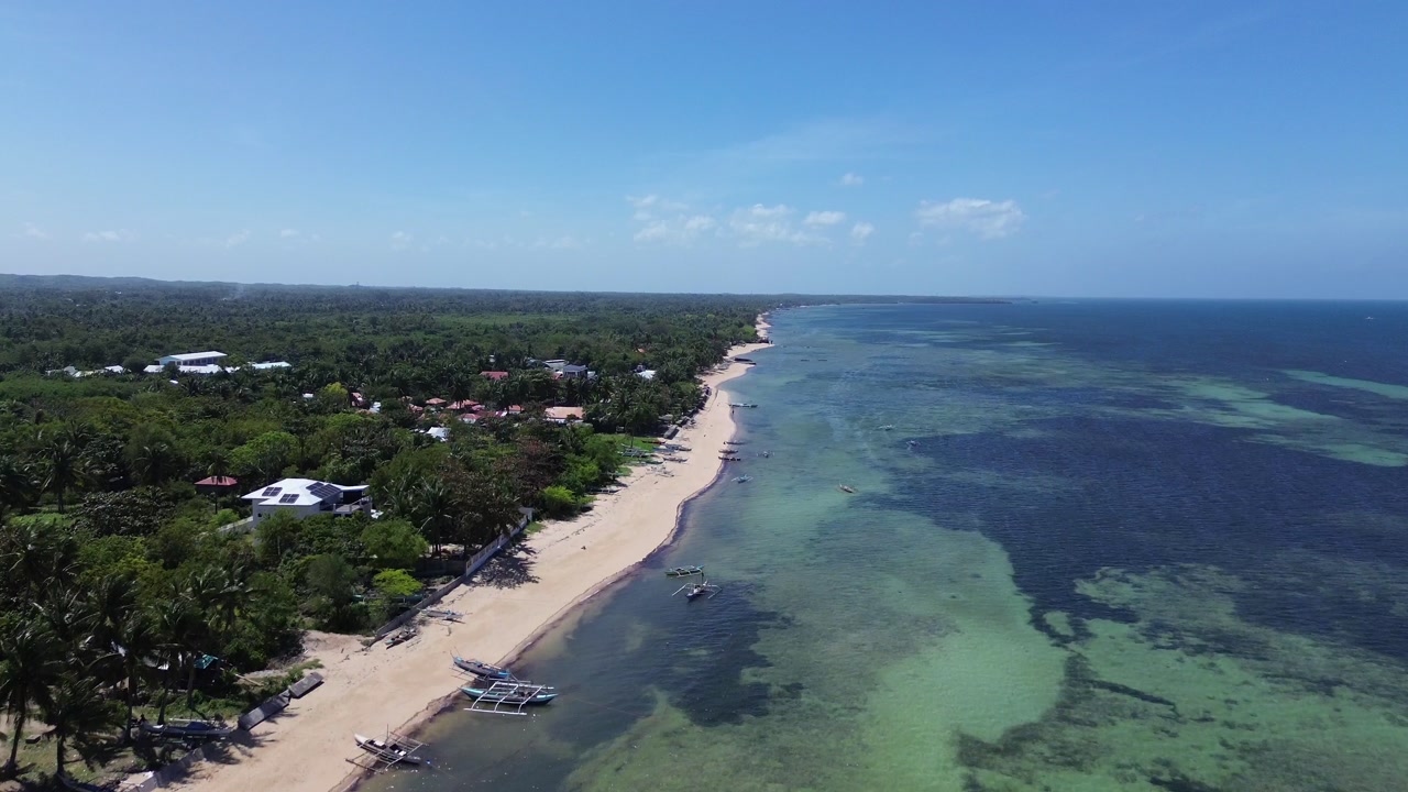 Aerial view of traditional Bangka boats anchored along a tropical shoreline with clear water and sandy beach surrounded by lush green vegetation on Bantayan Island Philippines Southeast Asia