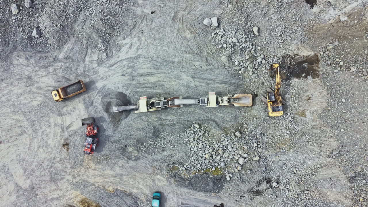 Workers extract granite in a busy quarry surrounded by machinery and piles of rocks in the daytime
