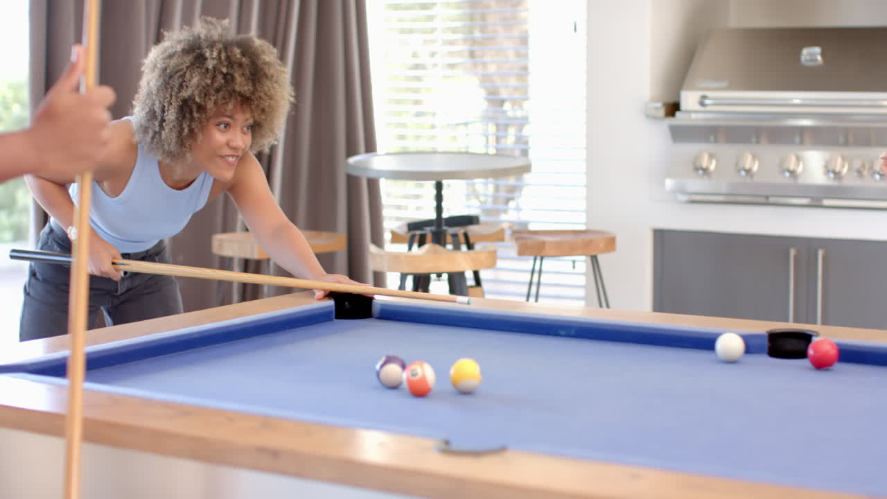 Playing pool, woman aiming cue stick at billiard balls on table with Diverse friends