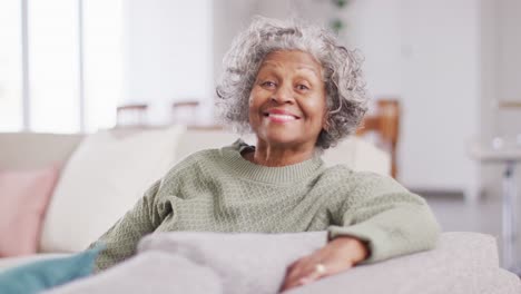 portrait of happy senior african american woman sitting on sofa, looking at camera and smiling