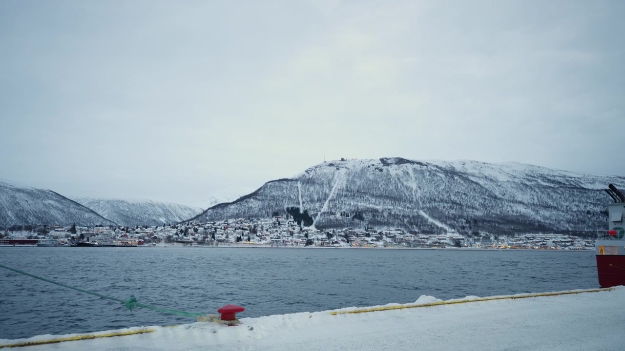 Schneebedeckte Berge gegenüber dem Hafen von Tromsø bei bedecktem Wintertageslicht, weite statische Aufnahme
