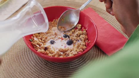Video-of-african-american-man-pouring-milk-into-bowl-of-meusli-at-breakfast-table