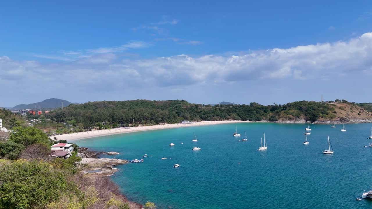 드론 영상은 태국 푸켓의 조용한 만을 포착합니다. 은 하늘 아래 선박, 울창한 초록색, 은 파란 물을 보여줍니다.