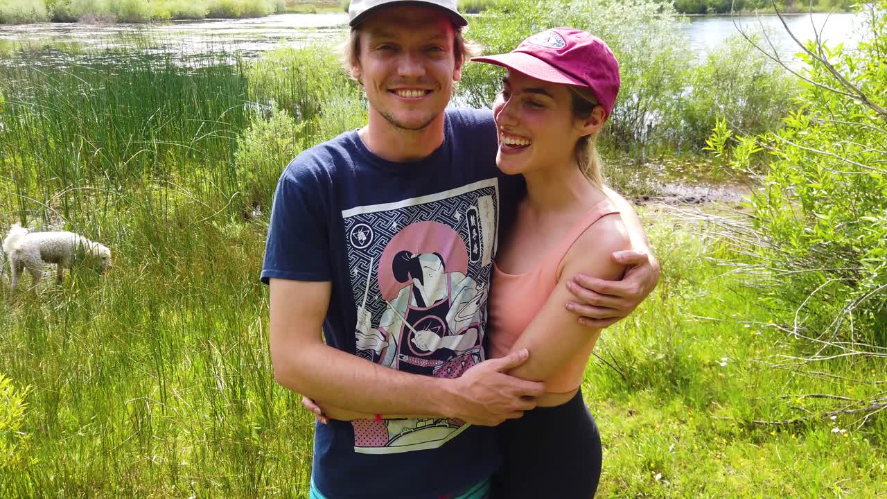 Um homem e uma mulher felizes e apaixonados se abraçam e beijam em uma caminhada com seus cães e sorriem em câmera lenta.