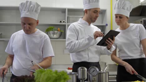 cocineros ocupados y chef de cocina consultando con la tableta