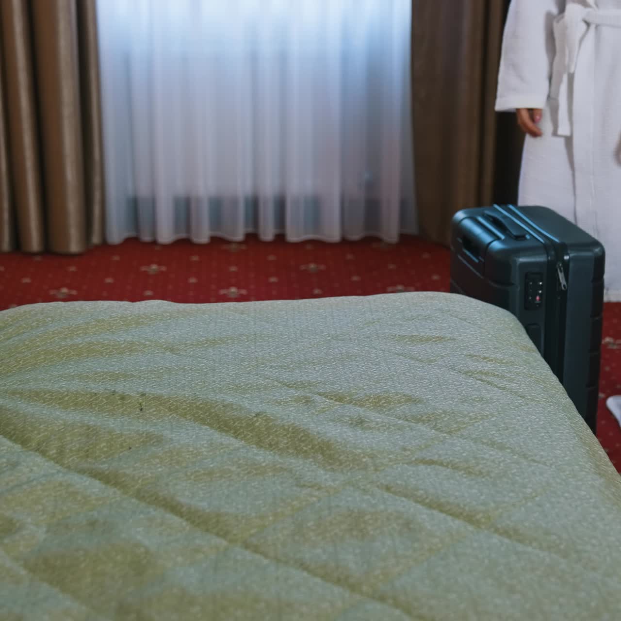 Couple in bedroom in hotel. Woman in white robe putting suitcase on bed while husband standing nearby. Slow motion