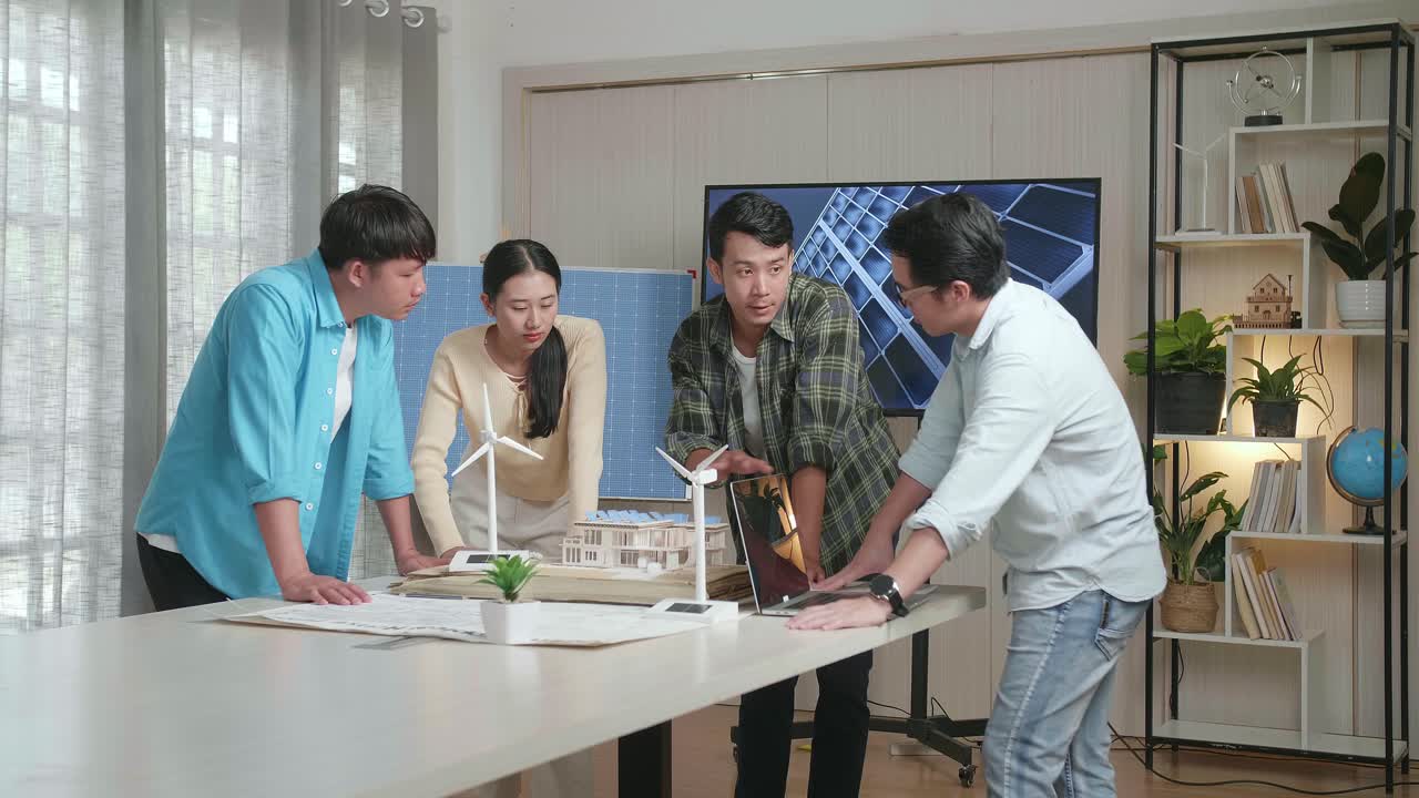 아시아 엔지니어 그룹이 사무실에서 태양 전지판을 가진 작은 집의 모델에 대해 회의를 하고 있습니다.