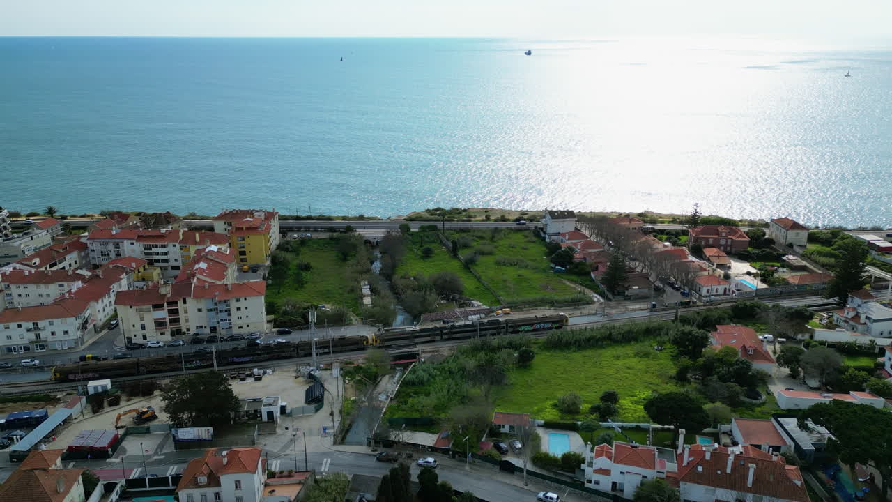 Aerial view tracking a train on the coastline of Estoril, in sunny Portugal