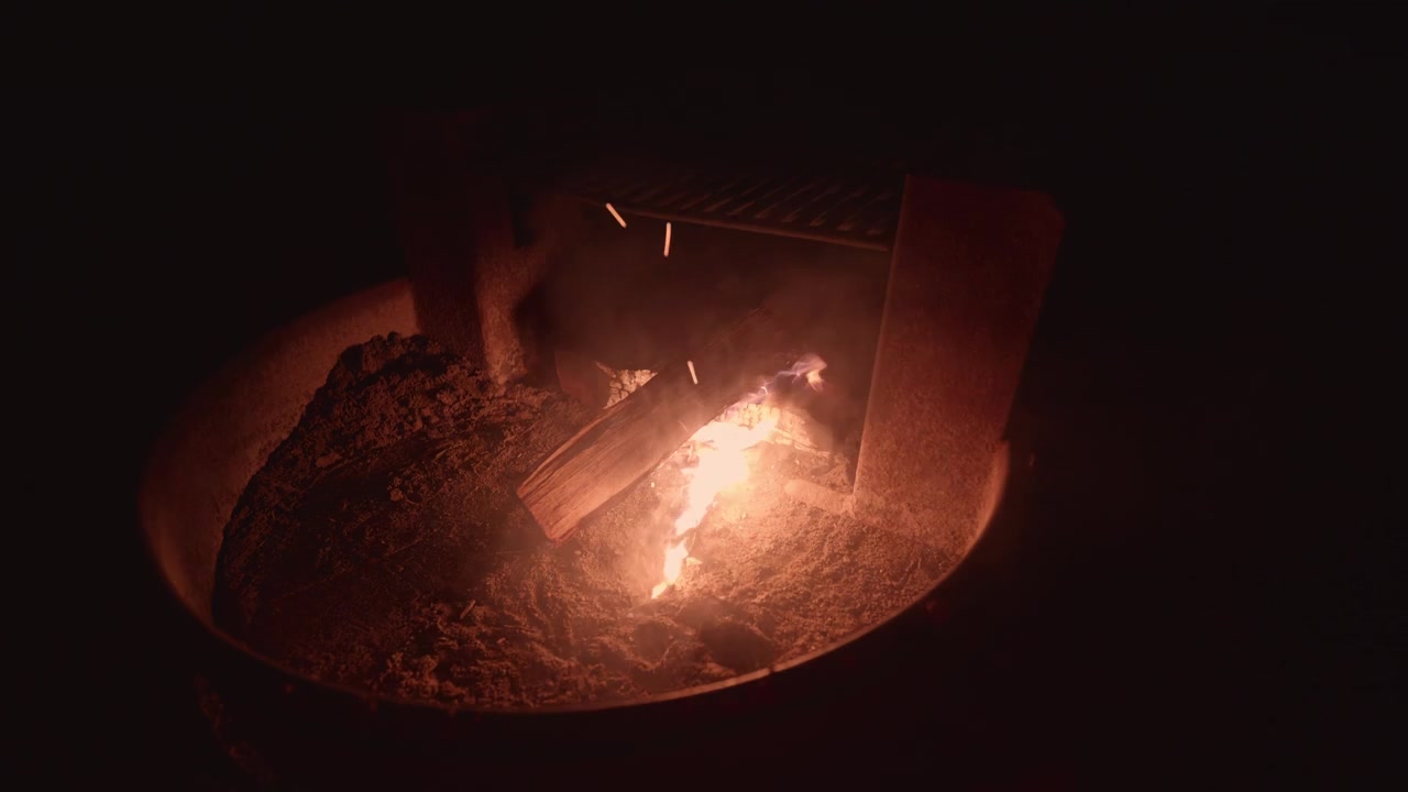Vedkubber knitrer og brenner i en metallbålpanne, og kaster et varmt skjær i mørket. Ideelt for camping eller innhold om utendørsliv.