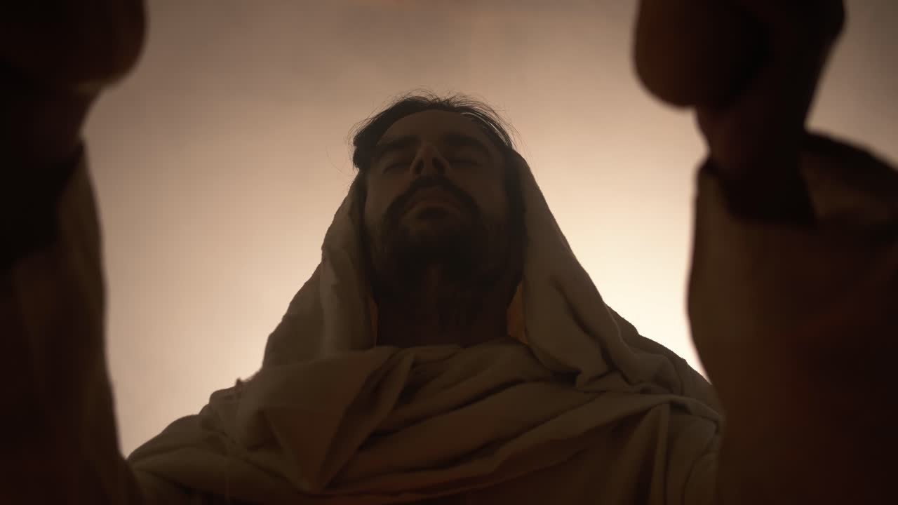 Jesus Christ in white hooded robe holding bread as he stands in glowing, bright light praying. Perfect for representation of Jesus as the bread of life, last supper, communion, Christian sacraments.