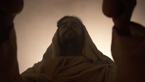 jesus christ in white hooded robe holding bread as he stands in glowing, bright light praying. perfect for representation of jesus as the bread of life, last supper, communion, christian sacraments.