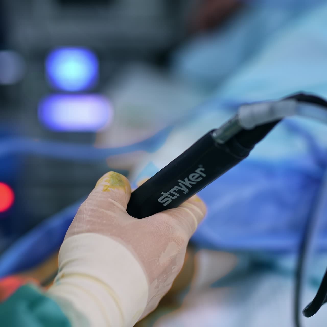 Surgeon's gloved hand holding a device tool. Doctor moving the surgical appliance slowly at surgery. Close up. Blurred backdrop