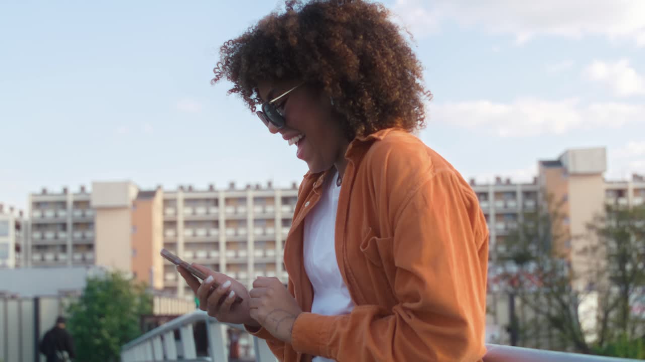 Black woman standing on the bridge and looking at her mobile phone