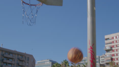 general shot of a young caucasian man playing street basketball by himself, shooting and making baskets, on a sunny day