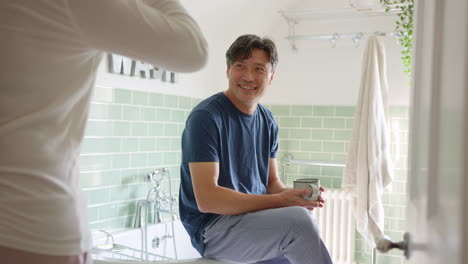 Mature-Asian-couple-wearing-pyjamas-sitting-in-bathroom-enjoying-morning-hot-drinks-together---shot-in-slow-motion