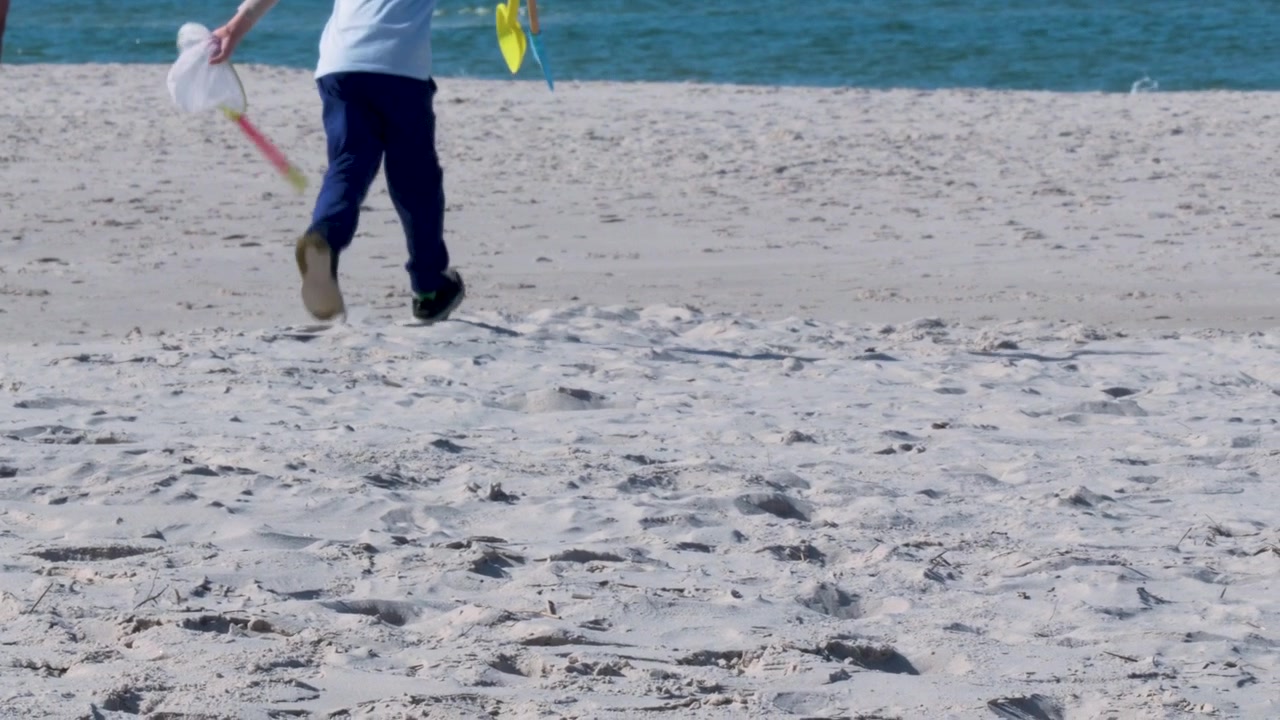 Un bambino cammina su una spiaggia di sabbia bianca a Osetnik, in Polonia, portando una rete e palette di plastica colorate verso l'acqua blu dell'oceano. Concetto autentico di vacanza in famiglia e benessere