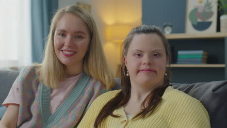 portrait of cheerful woman and girl with down syndrome at home