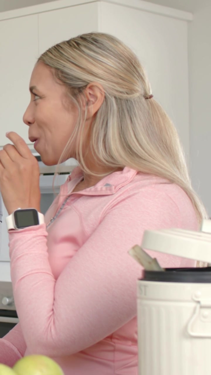 Video verticale: Donna sorridente che assaggia un cucchiaio dopo che il compagno ha parlato in cucina, con un pullover rosa.
