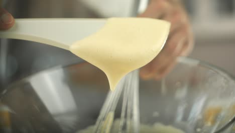 chef puts some egg yolk cream with a plastic spoon out of a glass bowl with an eggbeater and holds it up