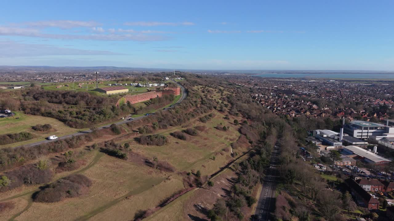 Fort Widley Portsmouth: Rivelazione di un forte militare riadattato e della sua posizione dominante sopra Portsmouth, con vista sull'entroterra su una campagna ondulata e una collina che digrada verso Portsmouth, illuminata da un sole dorato.