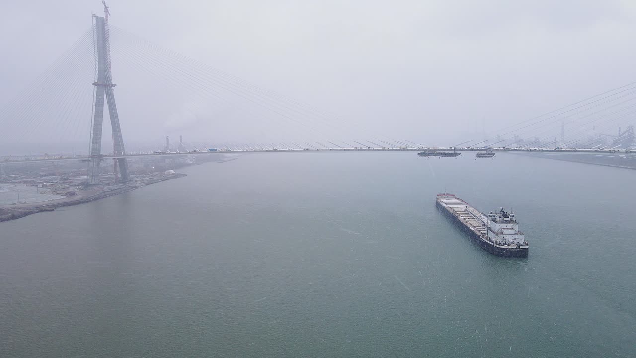 Drone video of Gordie Howe Bridge and cargo ship in snowy bay