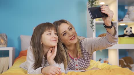 la niña y su madre están hablando por teléfono en la cama de la habitación del niño.