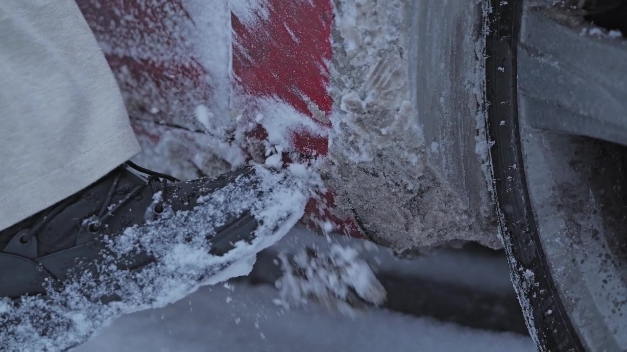 Manutenzione invernale al rallentatore che mostra la rimozione della neve ghiacciata dal passaruota di un veicolo.