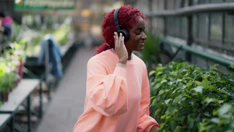 A-african-american-young-girl-in-colorful-blouse-and-headphones-is-dancing-in-flower-greenhouse