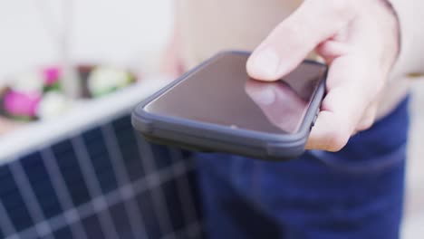 midsection of caucasian man holding solar panel and using smartphone