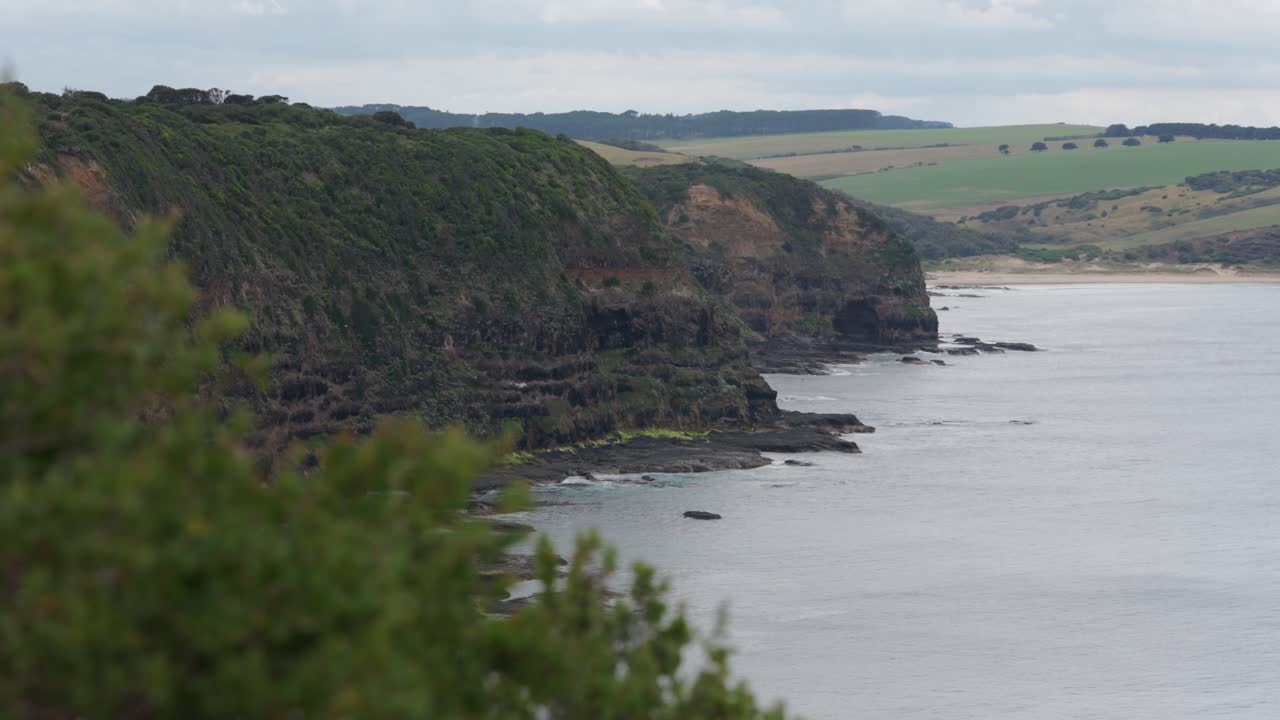 Wide shot of dramatic cliffs rising along the coastline, showcasing rugged terrain and the vast ocean beyond, highlighting nature's powerful and untamed beauty.